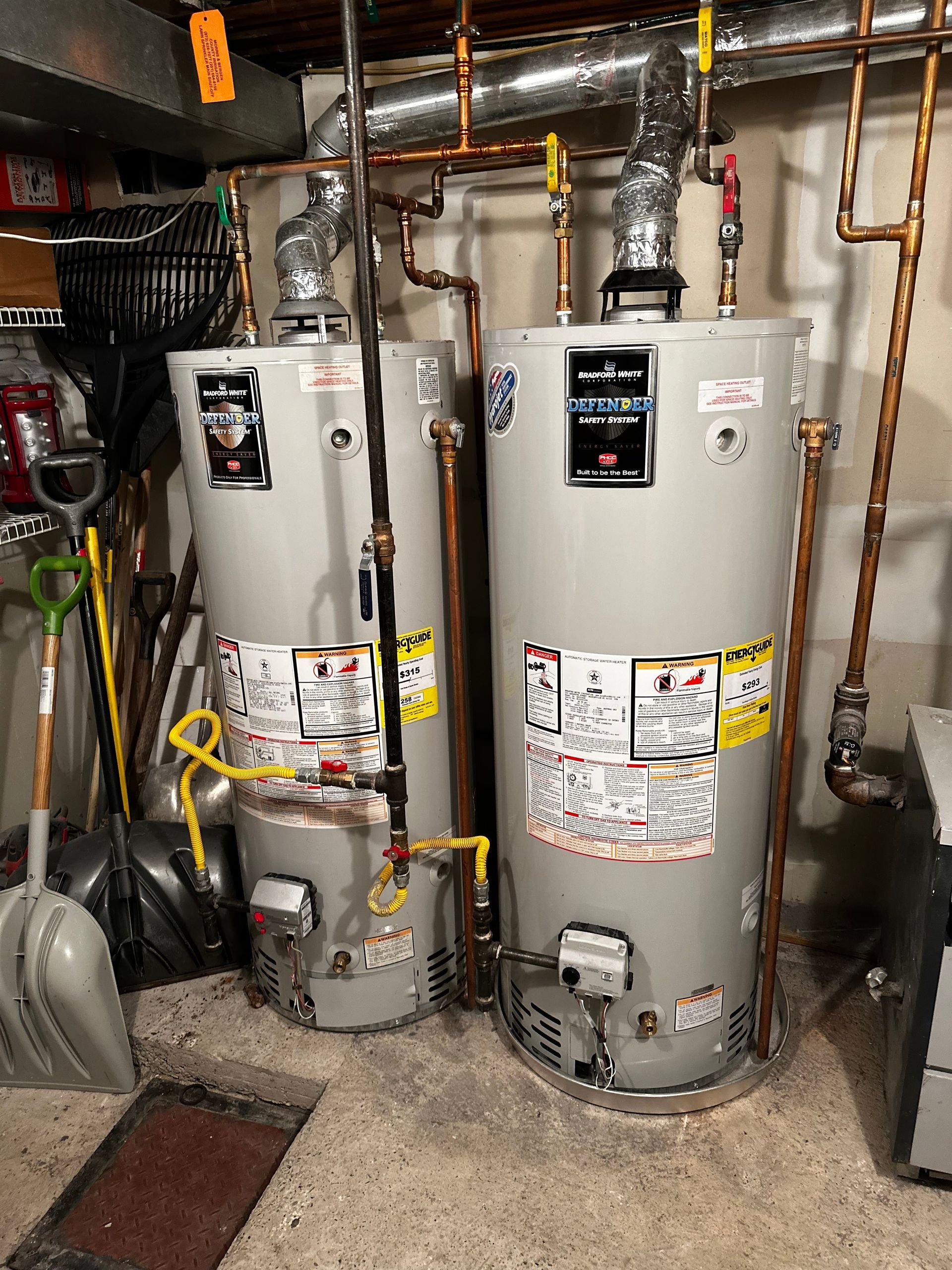 Two water heaters are sitting next to each other in a basement.