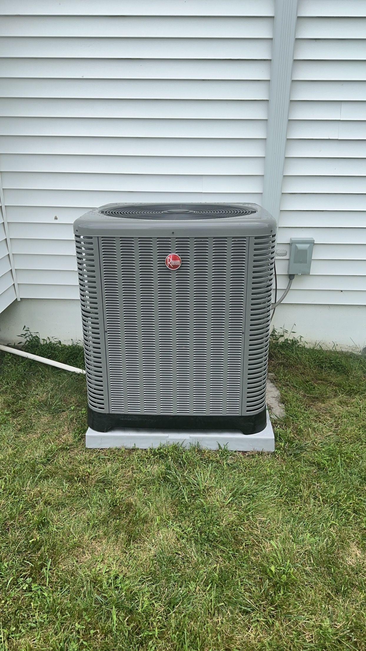 An air conditioner is sitting in the grass in front of a house.