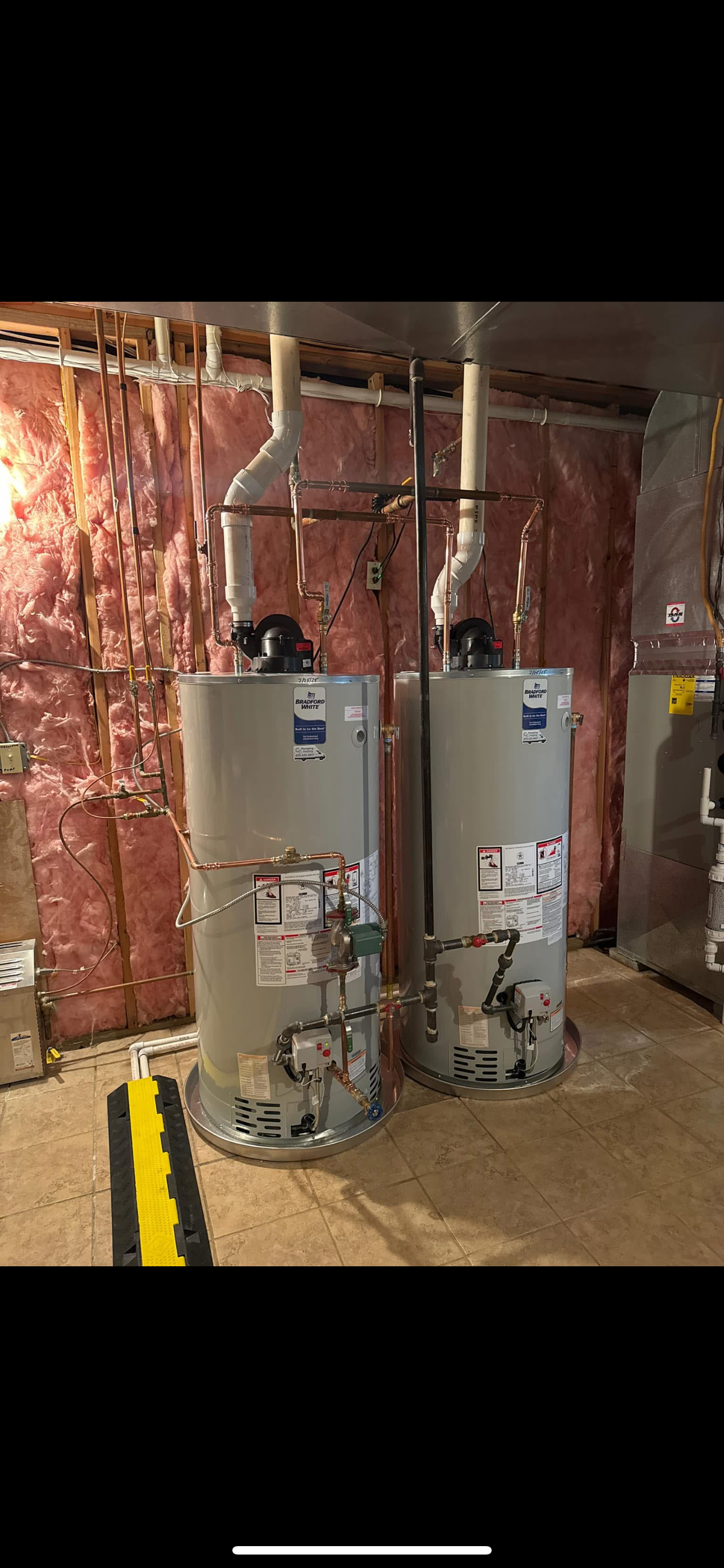 Two water heaters are sitting next to each other in a basement.