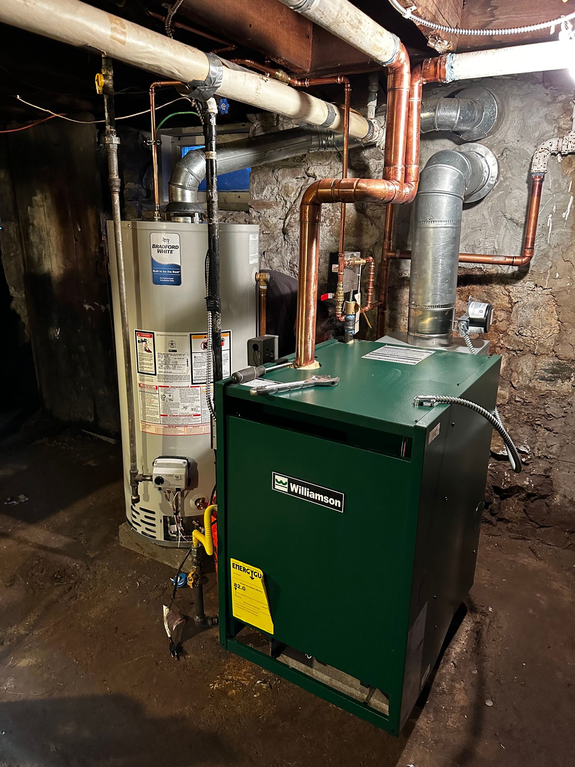 A green boiler is sitting in a basement next to a water heater.
