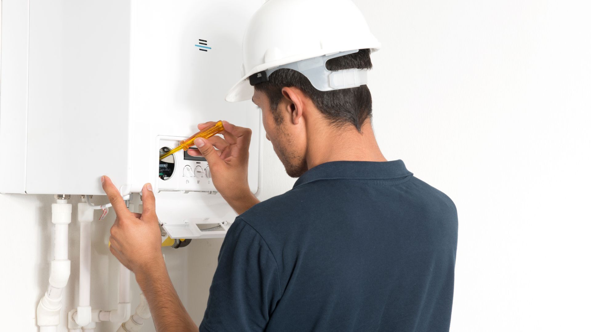 A man wearing a hard hat is measuring a boiler with a tape measure.