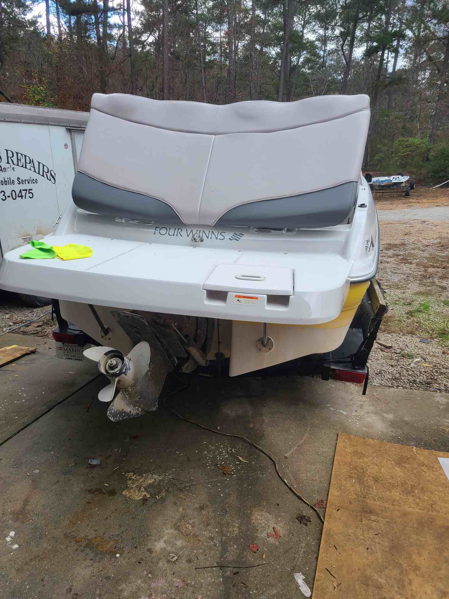 Rear view of a white and yellow boat with gray seating, propeller, and trailer.