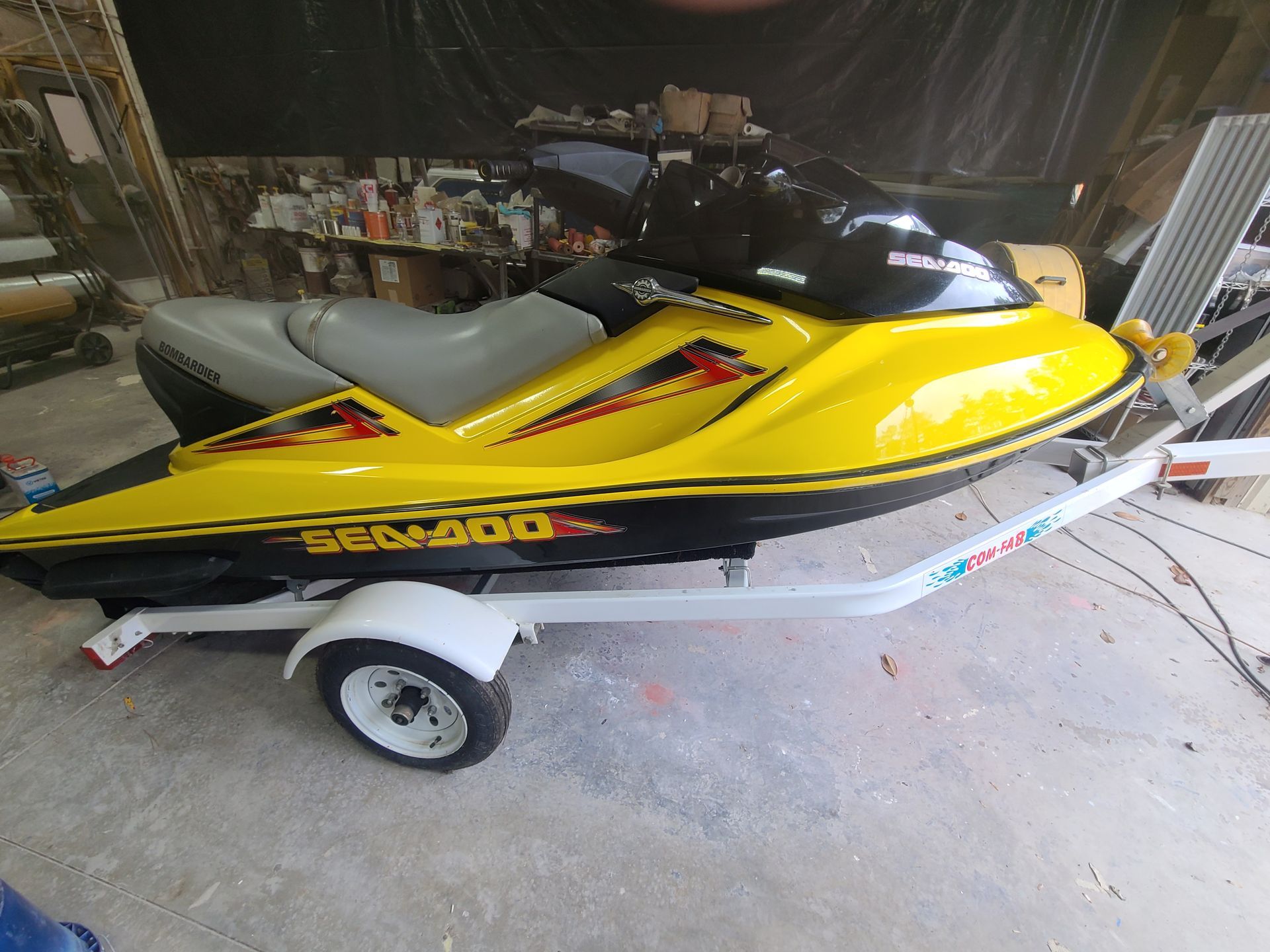 Sailboat hull on a wheeled cradle inside a workshop. Gray, with a black section on the bow.