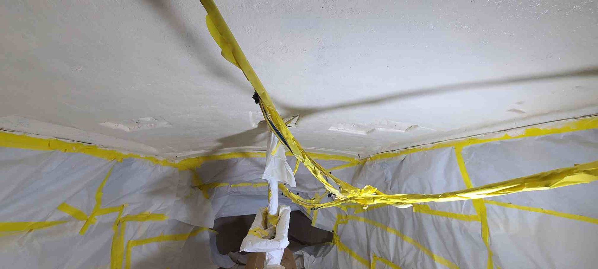 Ceiling and walls covered in plastic sheeting and yellow tape during a construction or remediation project.