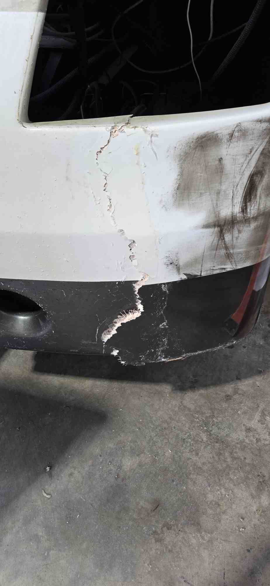 Damaged white car bumper with cracked paint and a missing section on a dark lower portion.