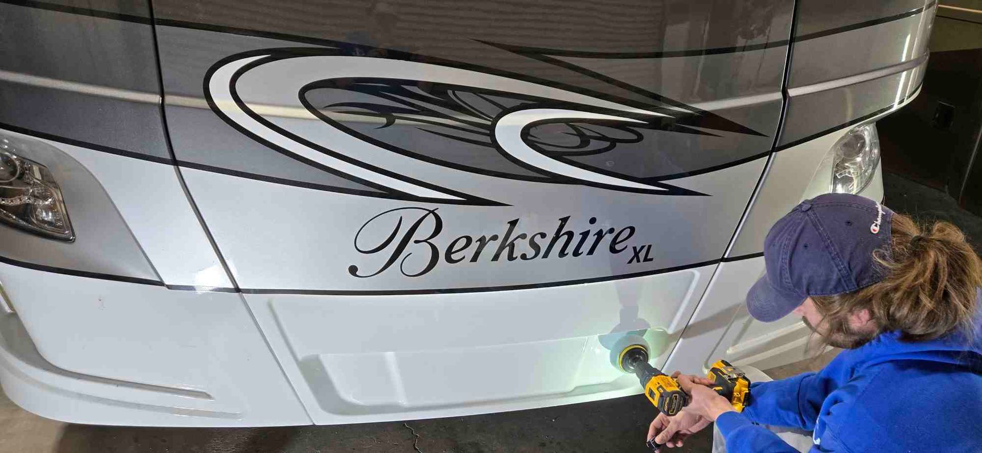 Man in blue gloves polishes a boat hull with a machine.