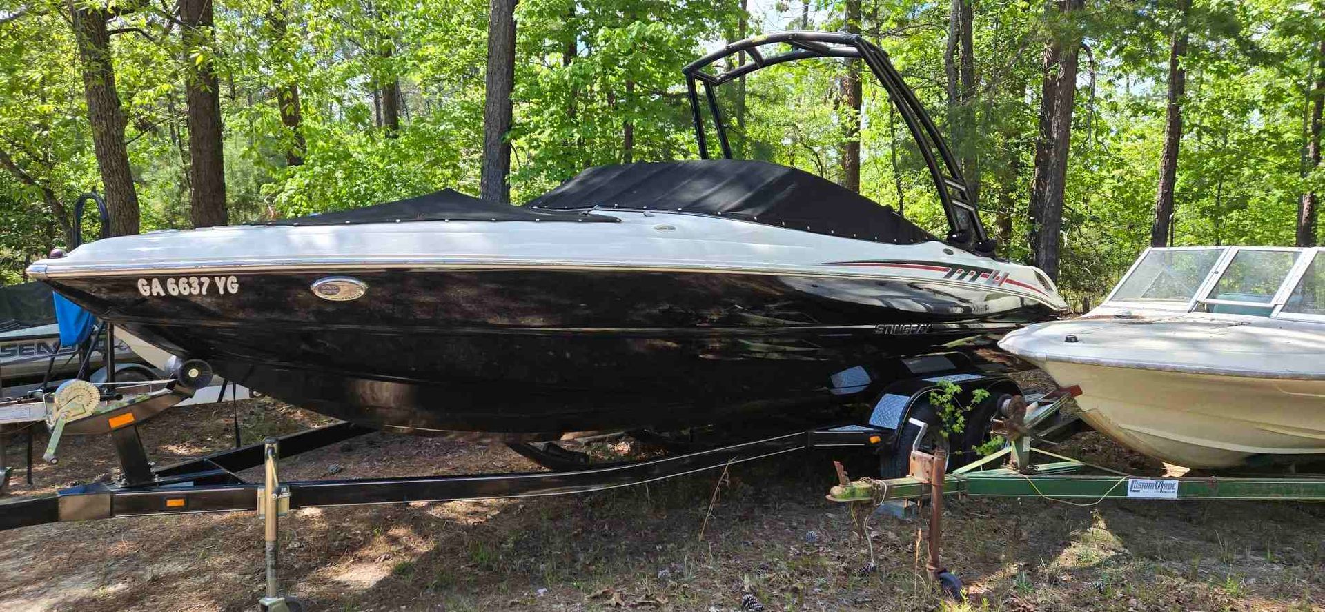 A boat hull on a stand inside a shed, showing construction or repair. The hull is mostly gray with a black stripe.