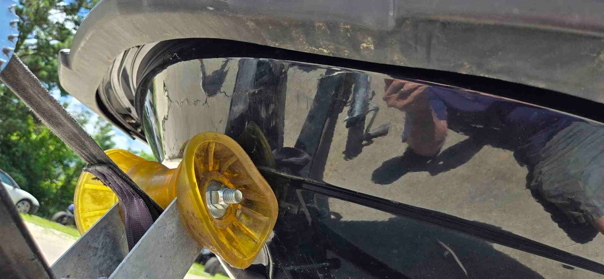 A person painting a boat's hull with a black roller, near the waterline, outdoors.