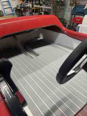 Interior of a red boat with gray and white striped flooring and a black steering wheel.