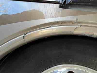 Damaged silver RV wheel well with visible cracks and a black tire.