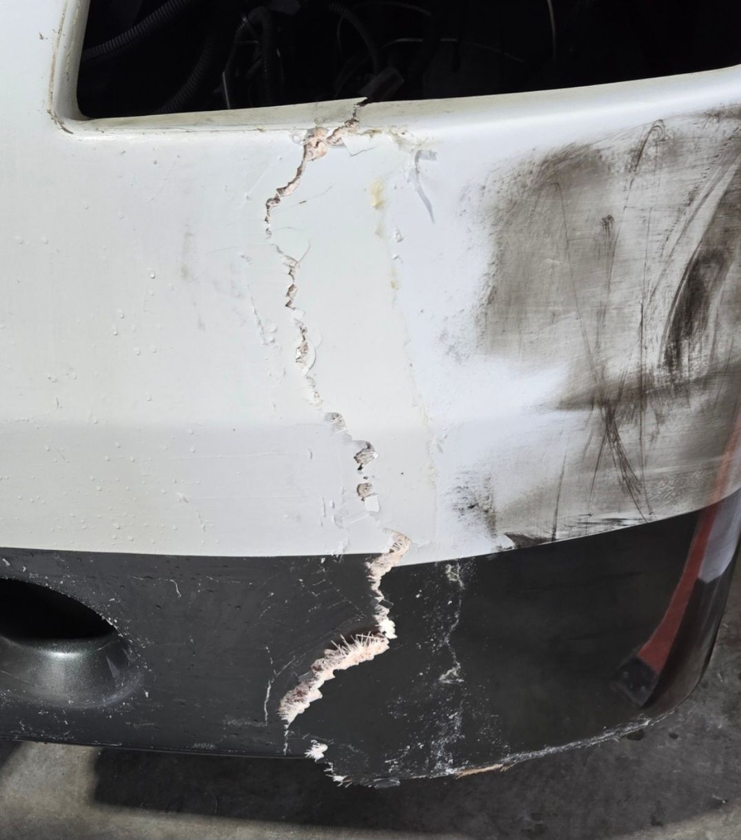 Damaged white car bumper with a large crack and dirt streaks.