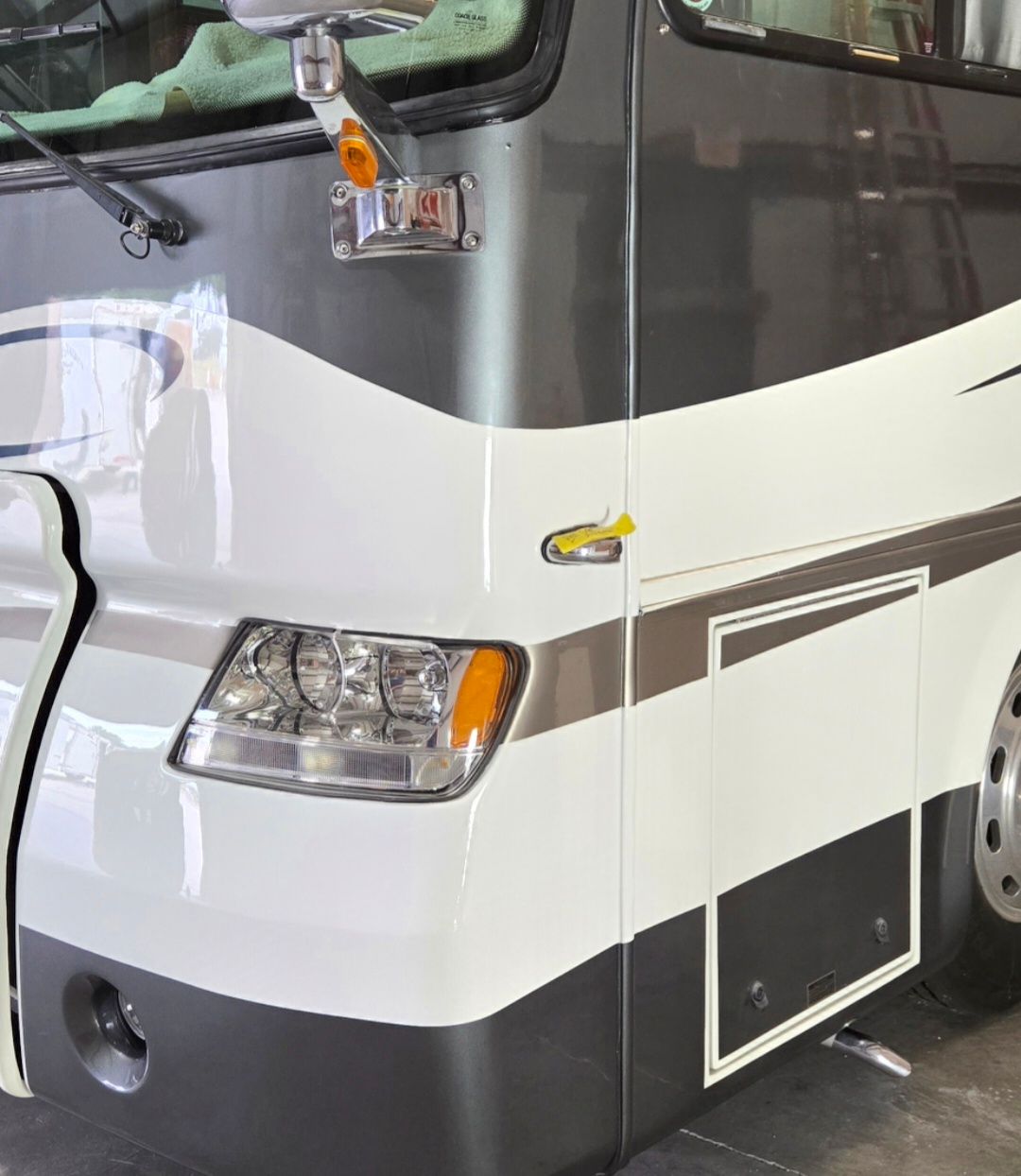White and gray RV exterior showing a headlight, side mirror, and decorative trim.