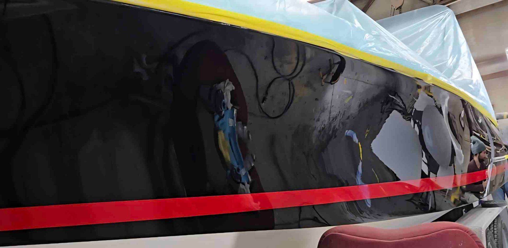 Boat hull partially covered in plastic, with a red stripe and Statue of Liberty detail.