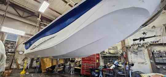 A boat is suspended in a workshop. The boat is white with a blue top. Tools and other equipment surround the boat.