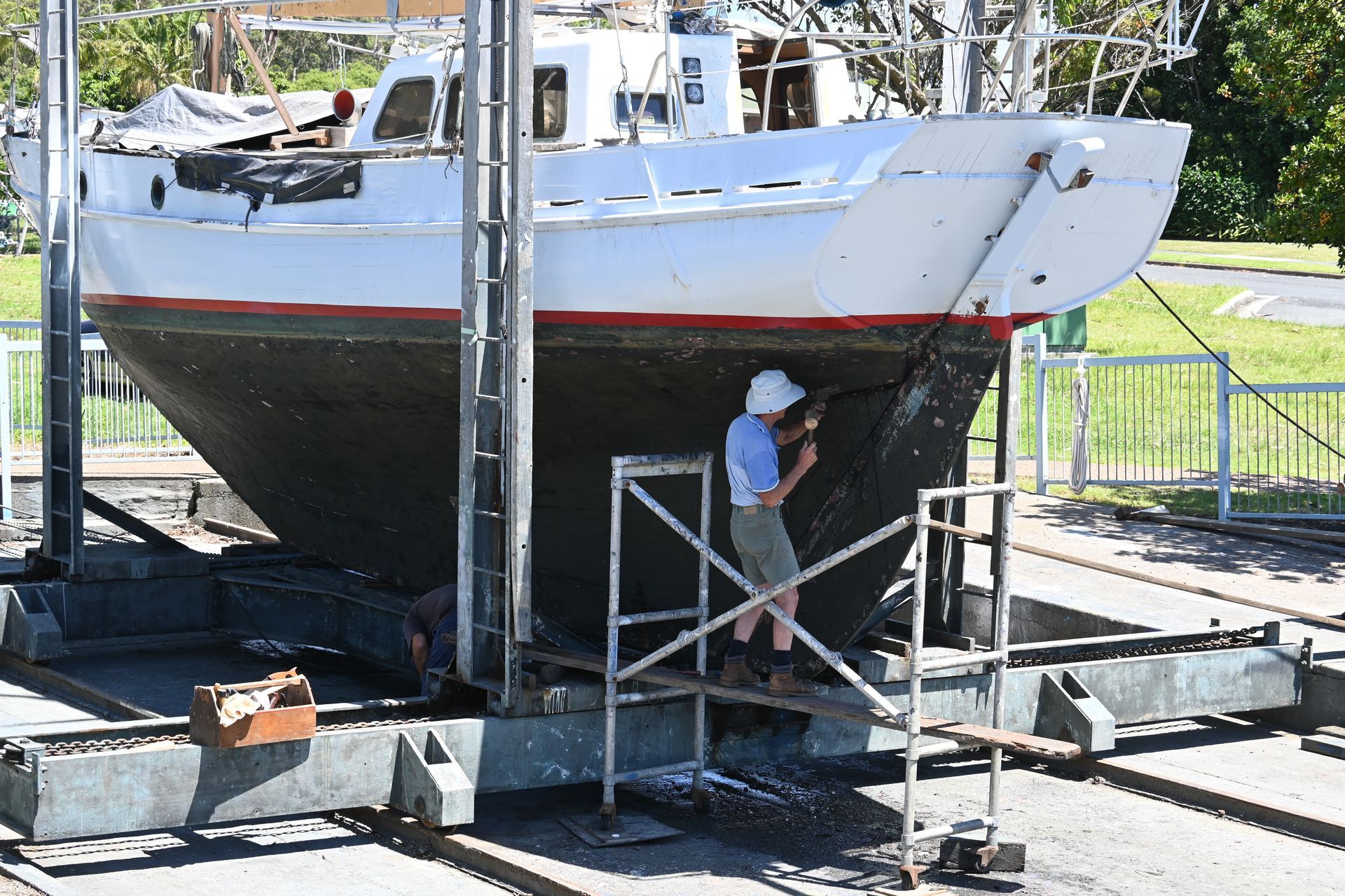 Person working on a white sailboat lifted by a boat hoist, outdoors.