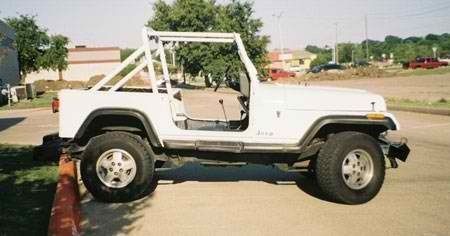 A white jeep with the door open is parked on the side of the road.