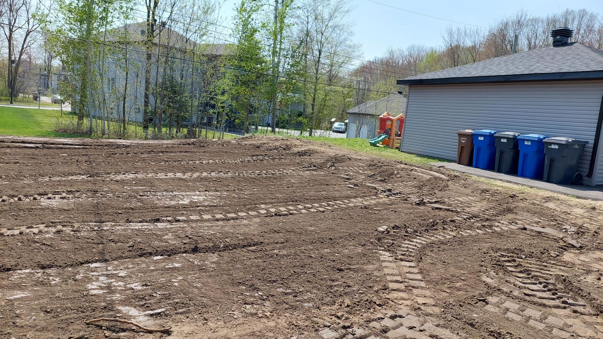 Un champ de terre avec une maison en arrière-plan et des poubelles au premier plan.