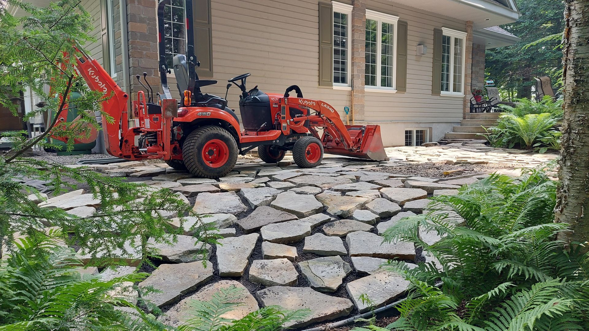 Un tracteur et une rétrocaveuse sont garés devant une maison.