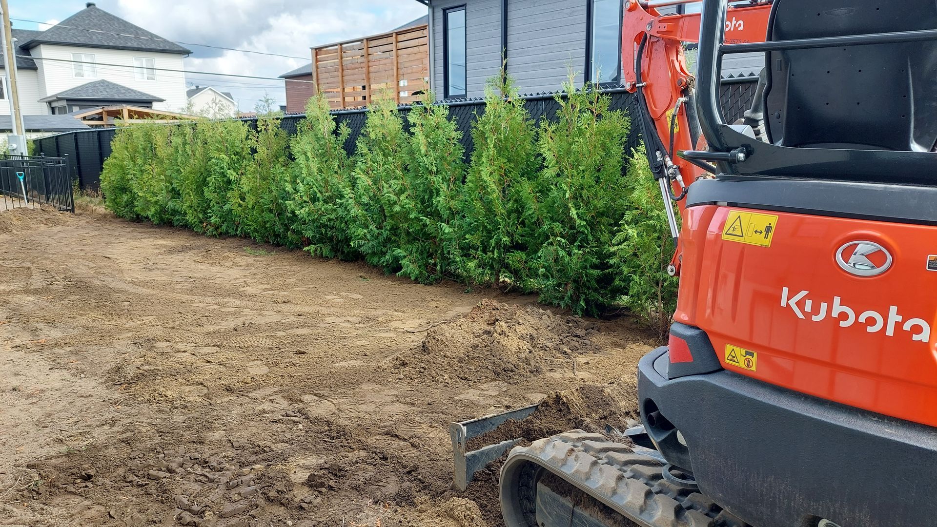 Une excavatrice rouge est assise dans la terre devant une maison.