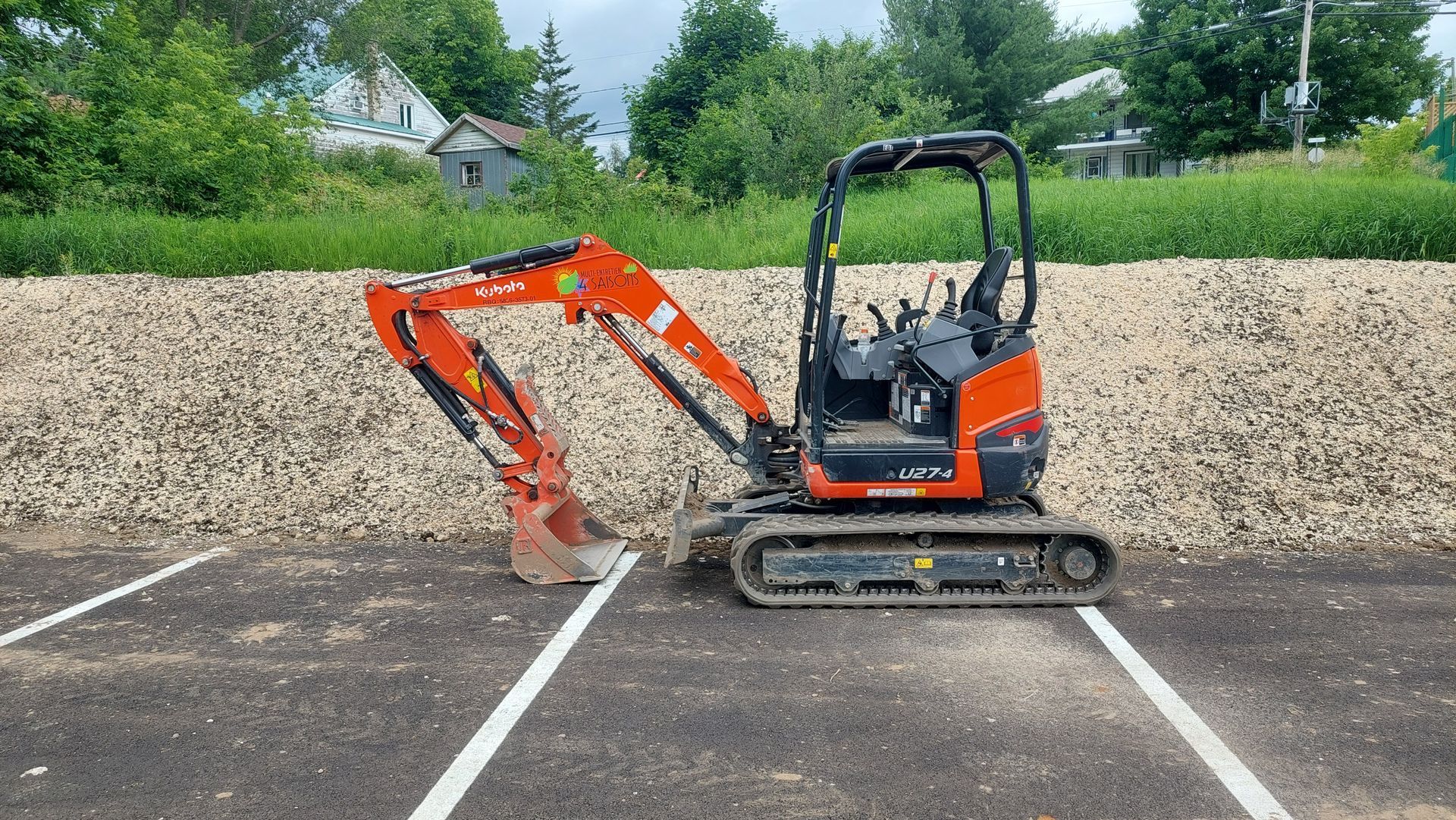 Une petite excavatrice rouge et noire est garée sur un parking.