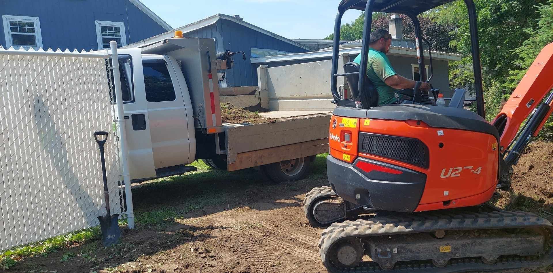 Un homme conduit une petite excavatrice à côté d'un camion à benne basculante.