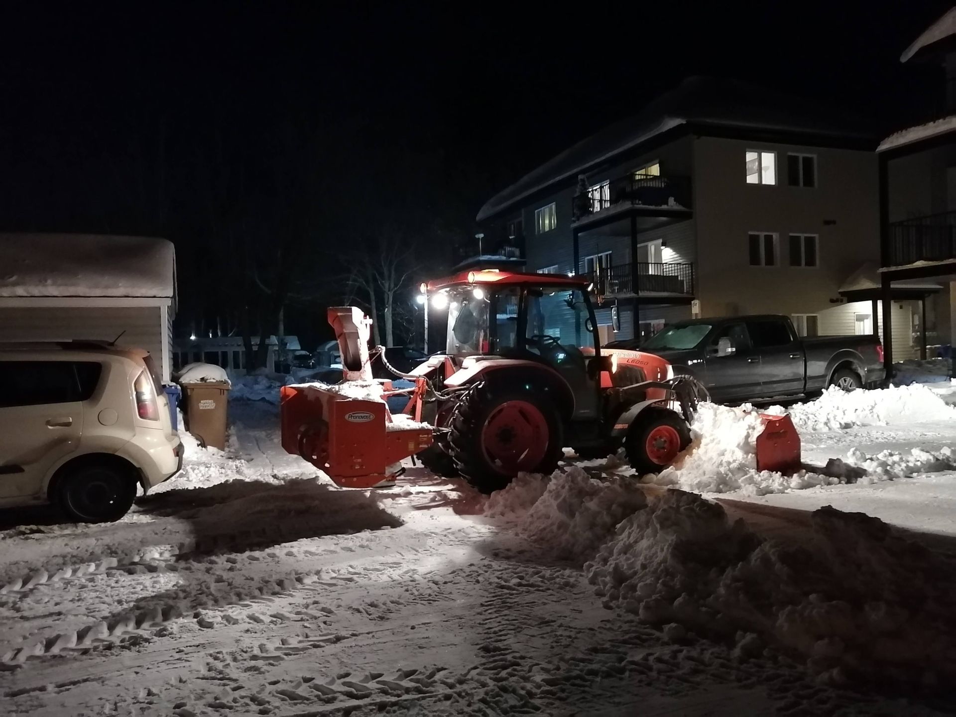 Un tracteur déneige un parking la nuit.