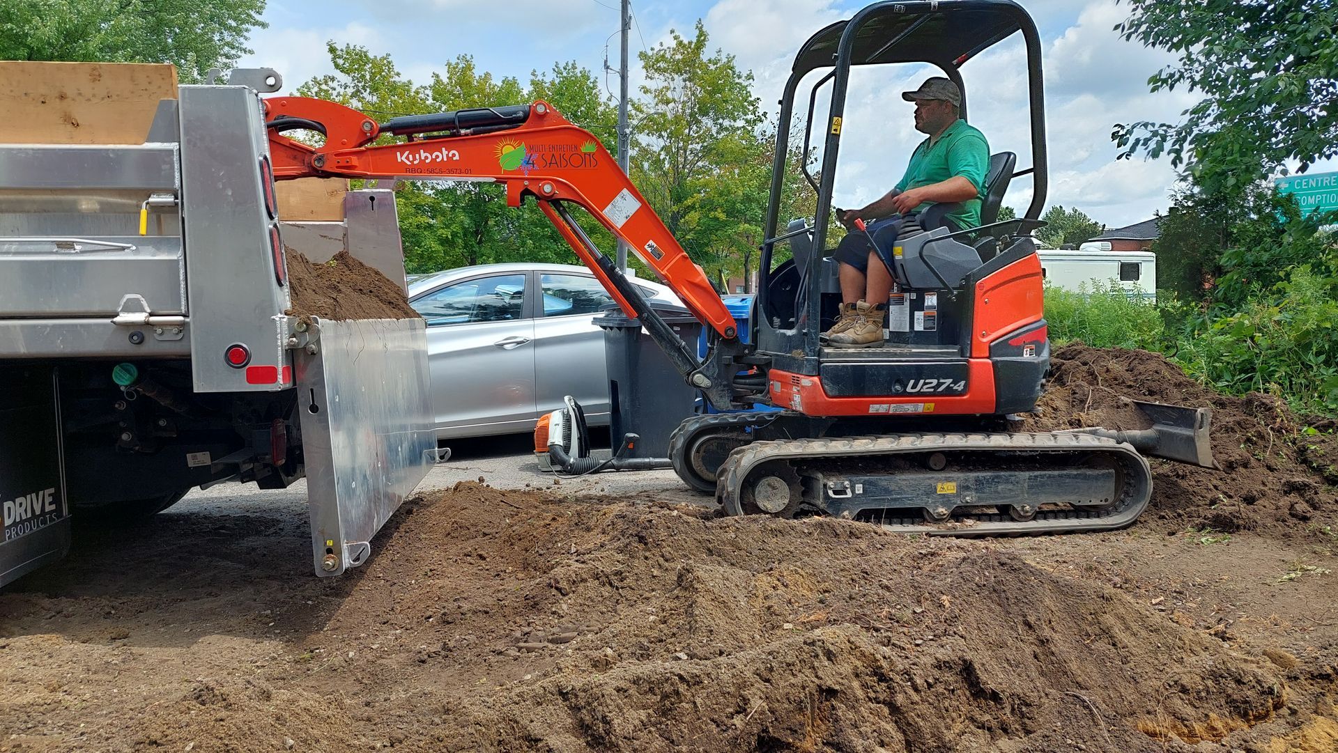Un homme conduit une petite excavatrice sur un chemin de terre.