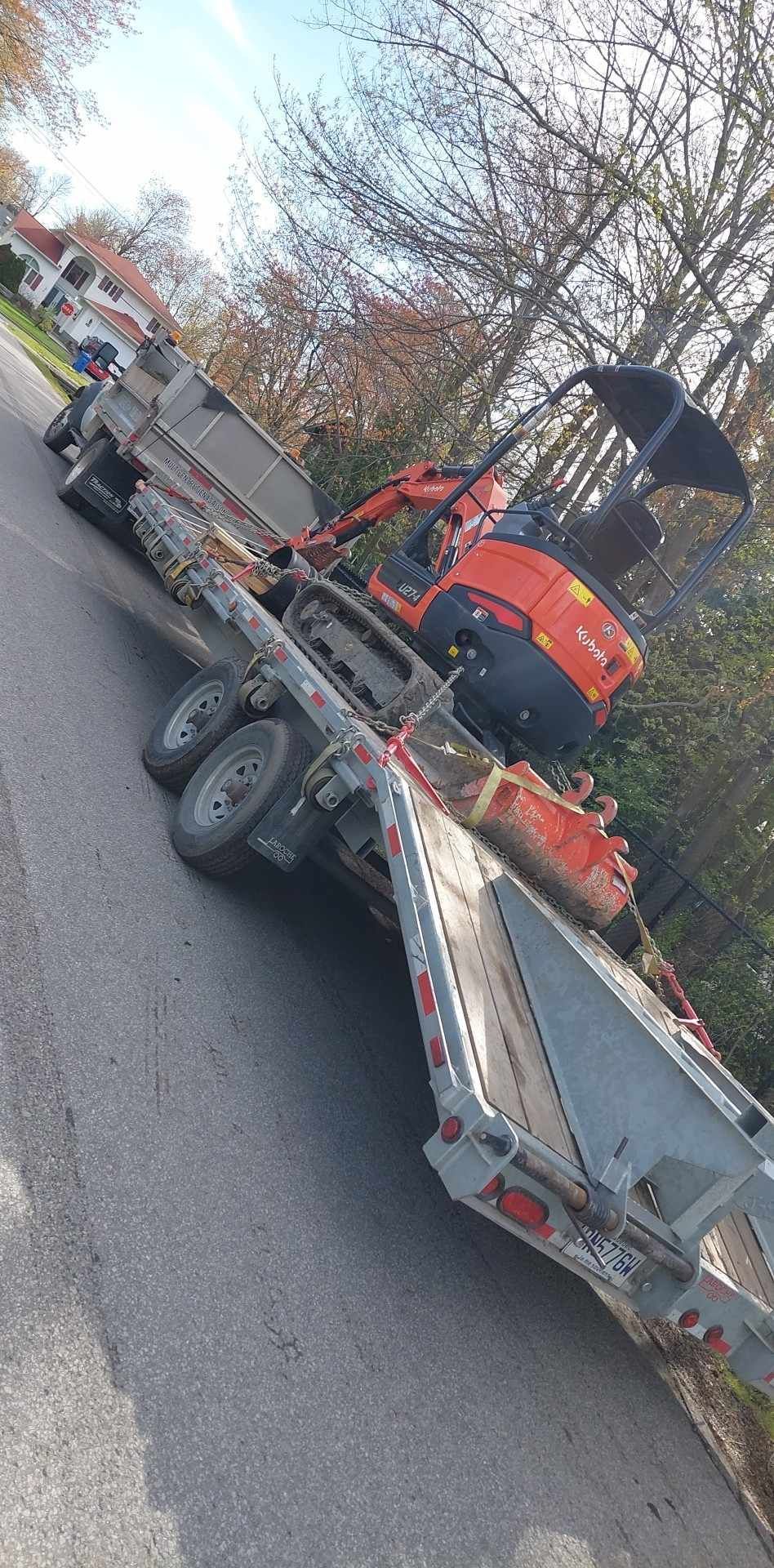 Une remorque avec une petite excavatrice dessus est garée sur le bord de la route.