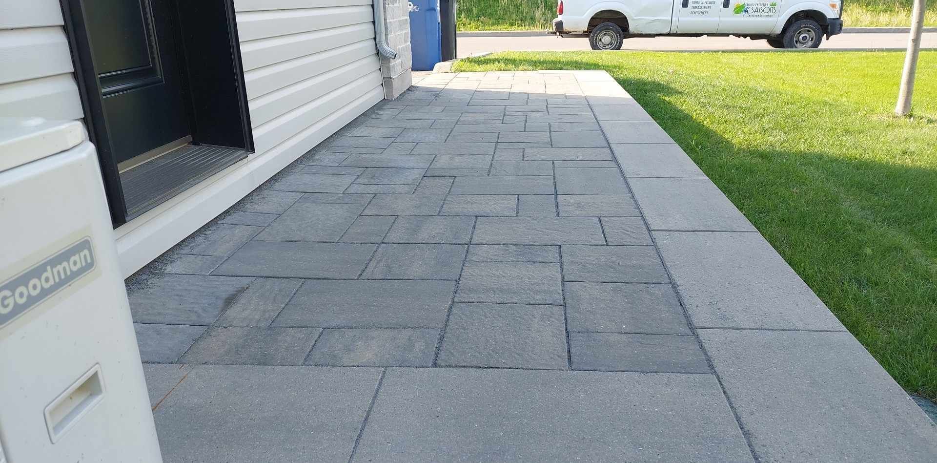 Un trottoir à côté d'une maison avec un camion blanc garé en arrière-plan.