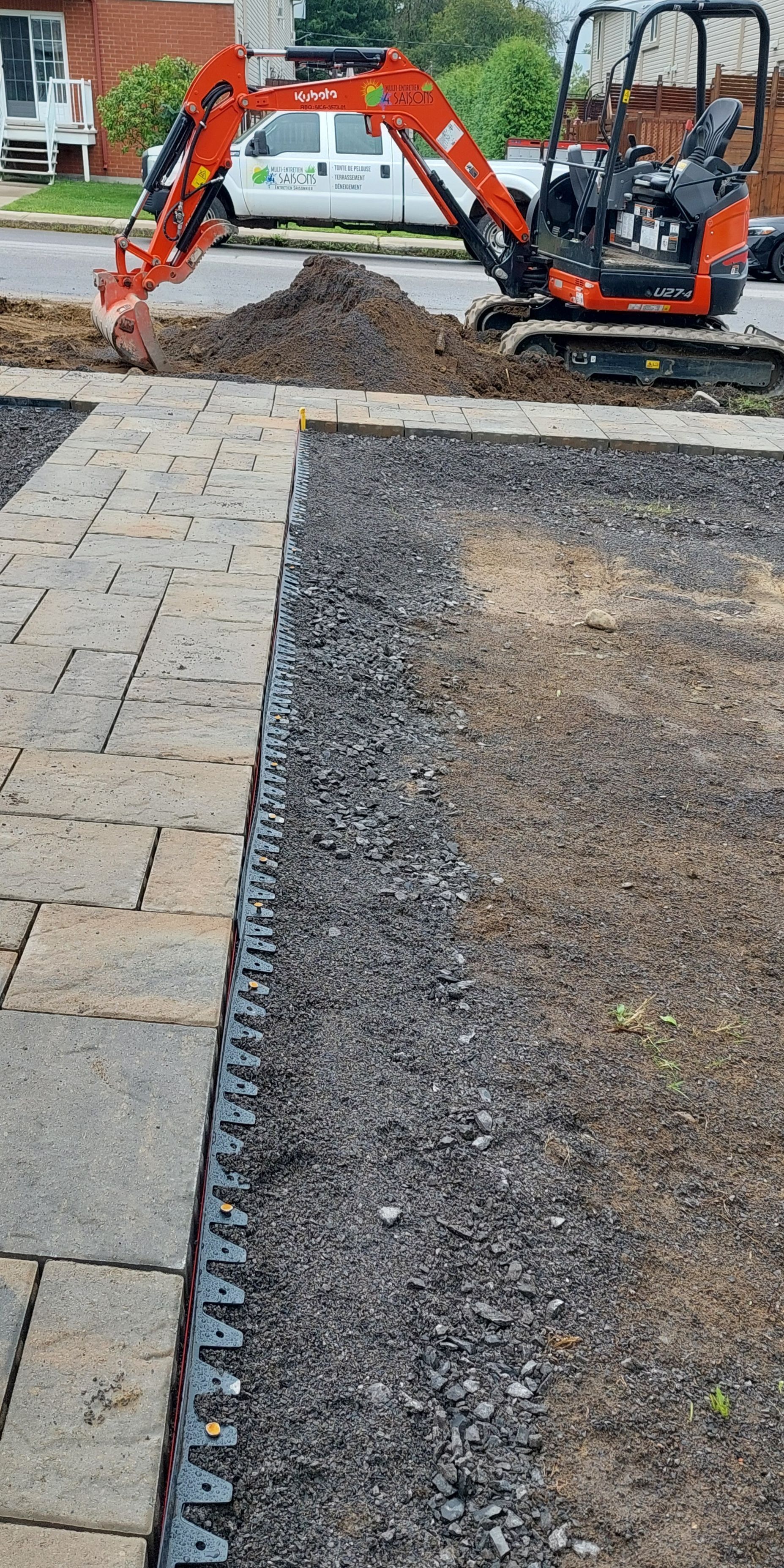 Une petite excavatrice creuse un trou dans le sol à côté d'un trottoir.