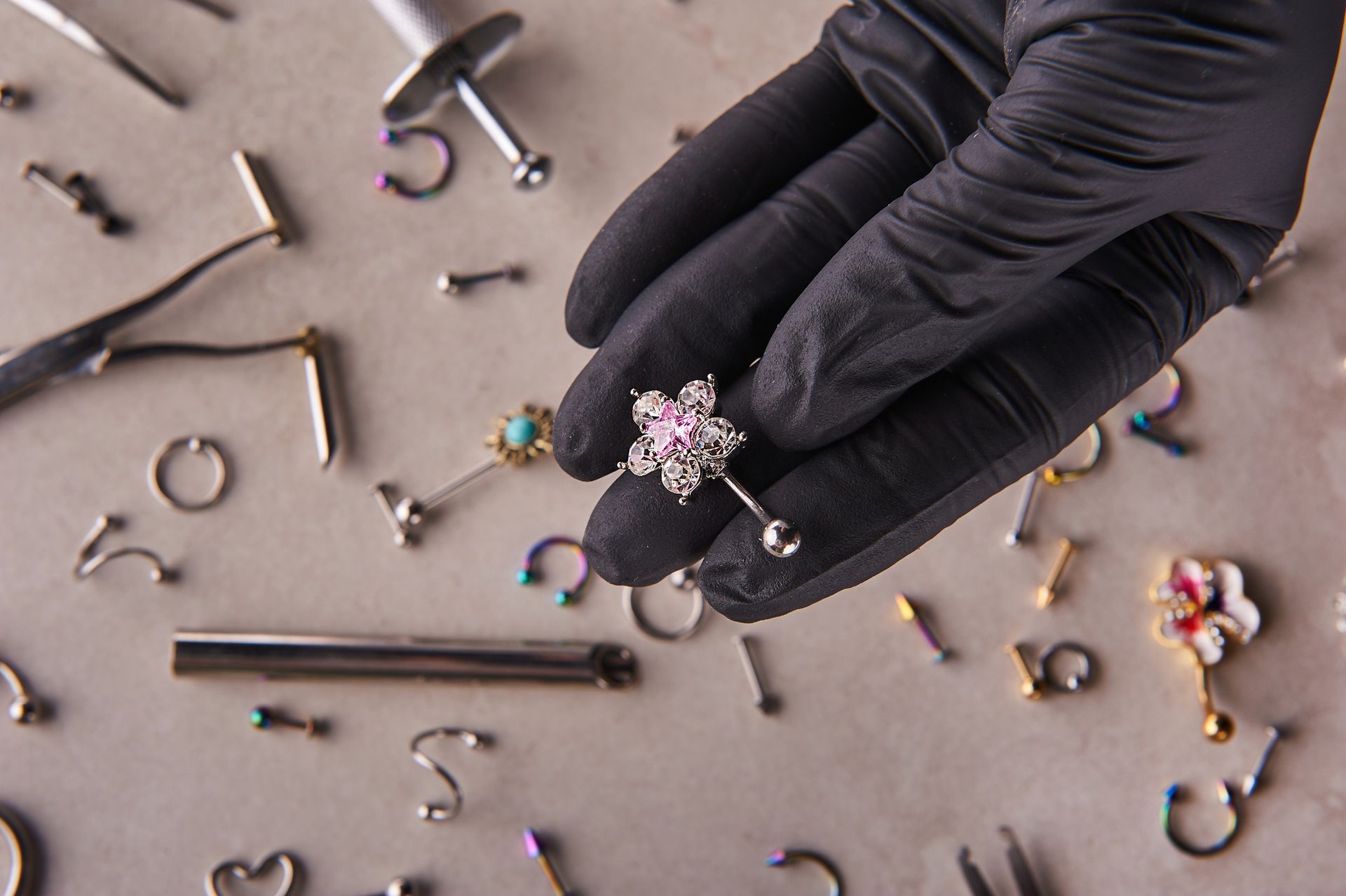 A person wearing black gloves is holding a piercing in their hand.