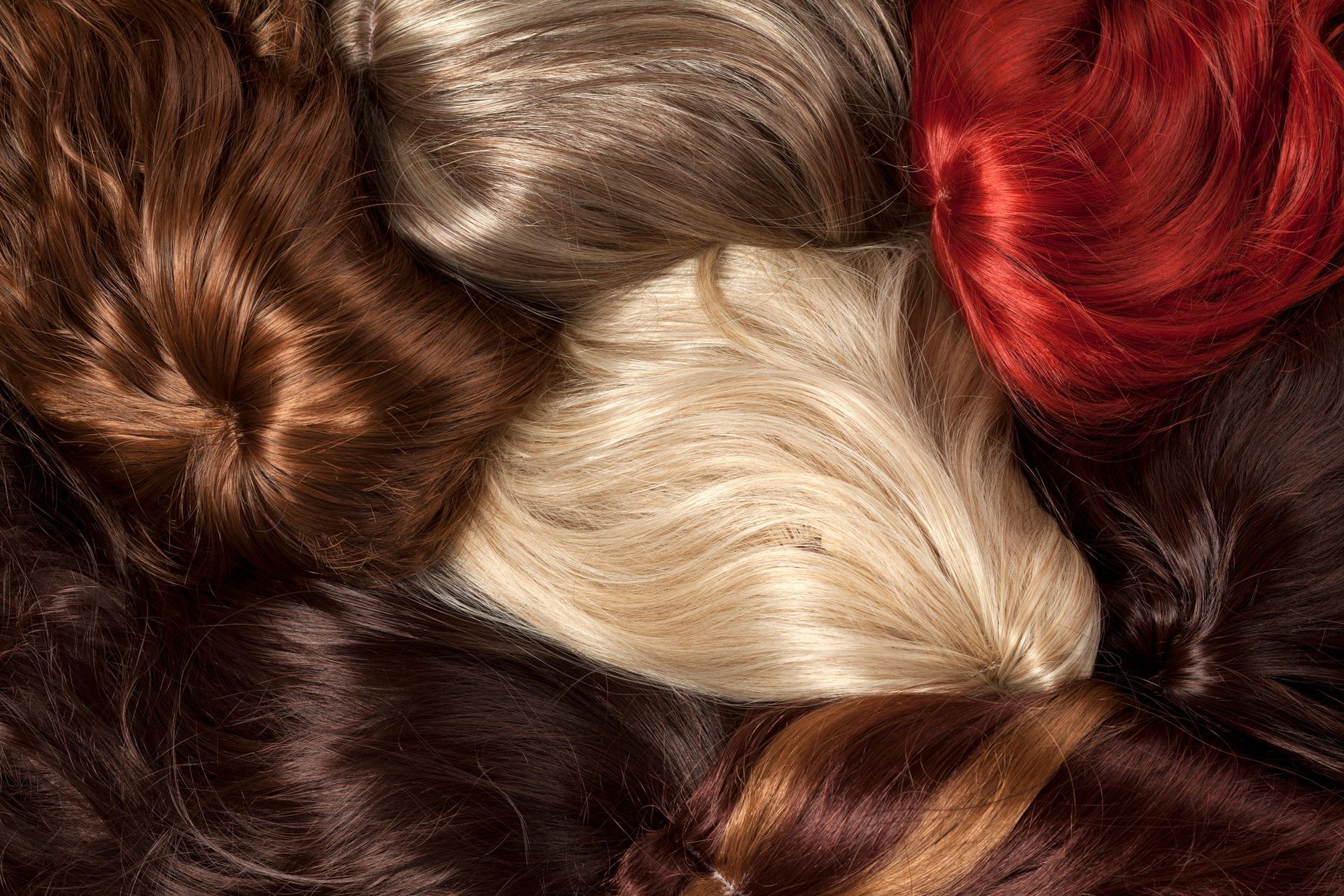 A bunch of different colored wigs are laying on top of each other.