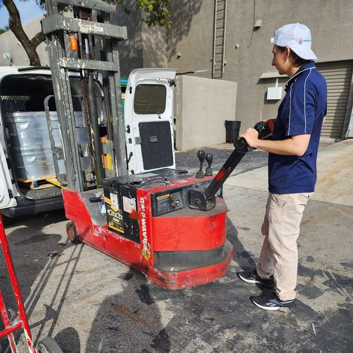 A man is pushing a red forklift in a parking lot