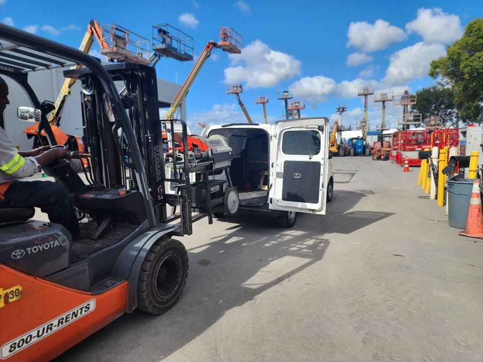 A man is driving a forklift in a parking lot next to a van.