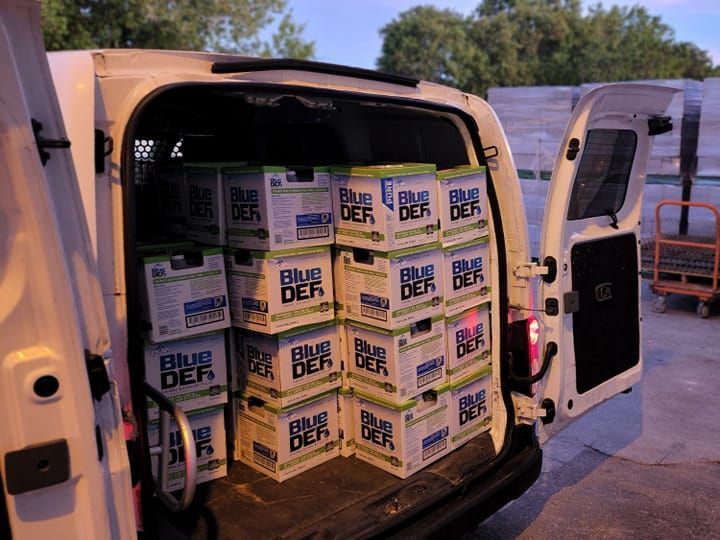 The back of a white van is filled with boxes of blue def batteries.