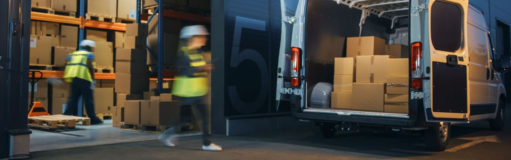 Two delivery vans are parked in front of a warehouse at night.