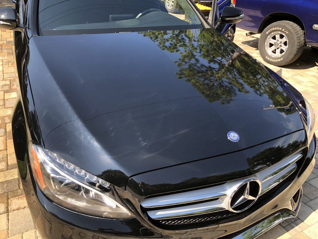 A black mercedes benz is parked in a driveway next to a blue truck.