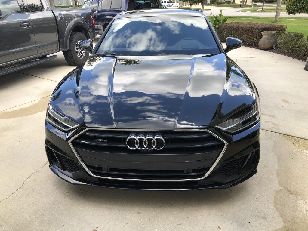 A black audi a7 is parked in a driveway next to a truck.