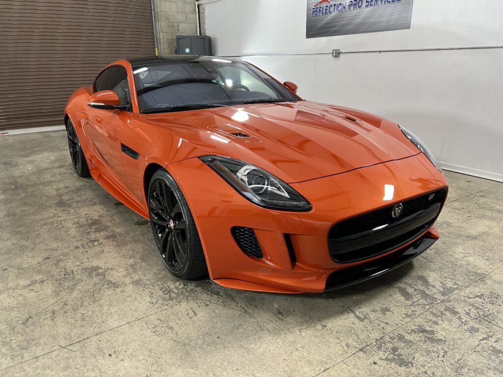 An orange jaguar f type is parked in a garage.