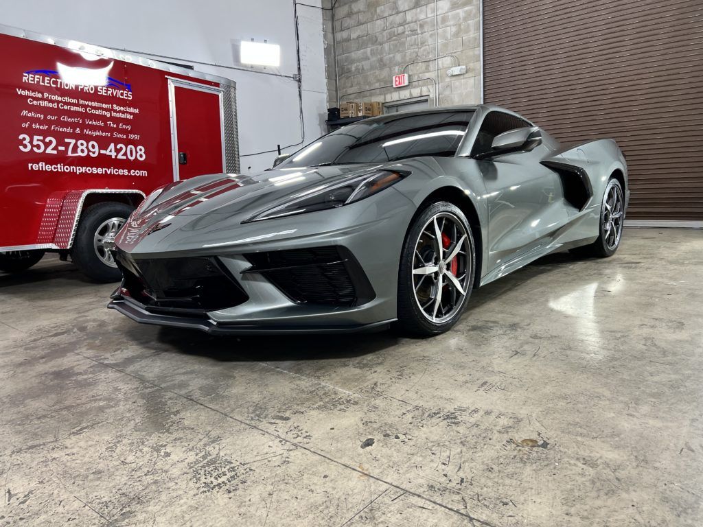 A gray corvette is parked in a garage next to a red trailer.