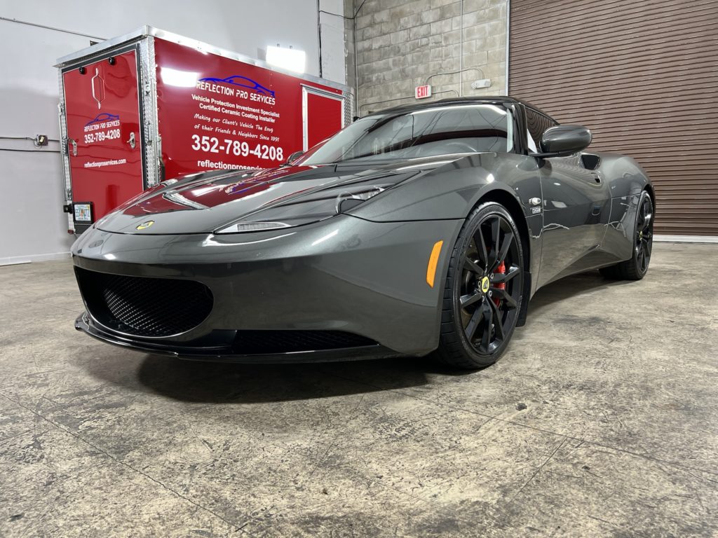 A gray sports car is parked in a garage next to a red truck.