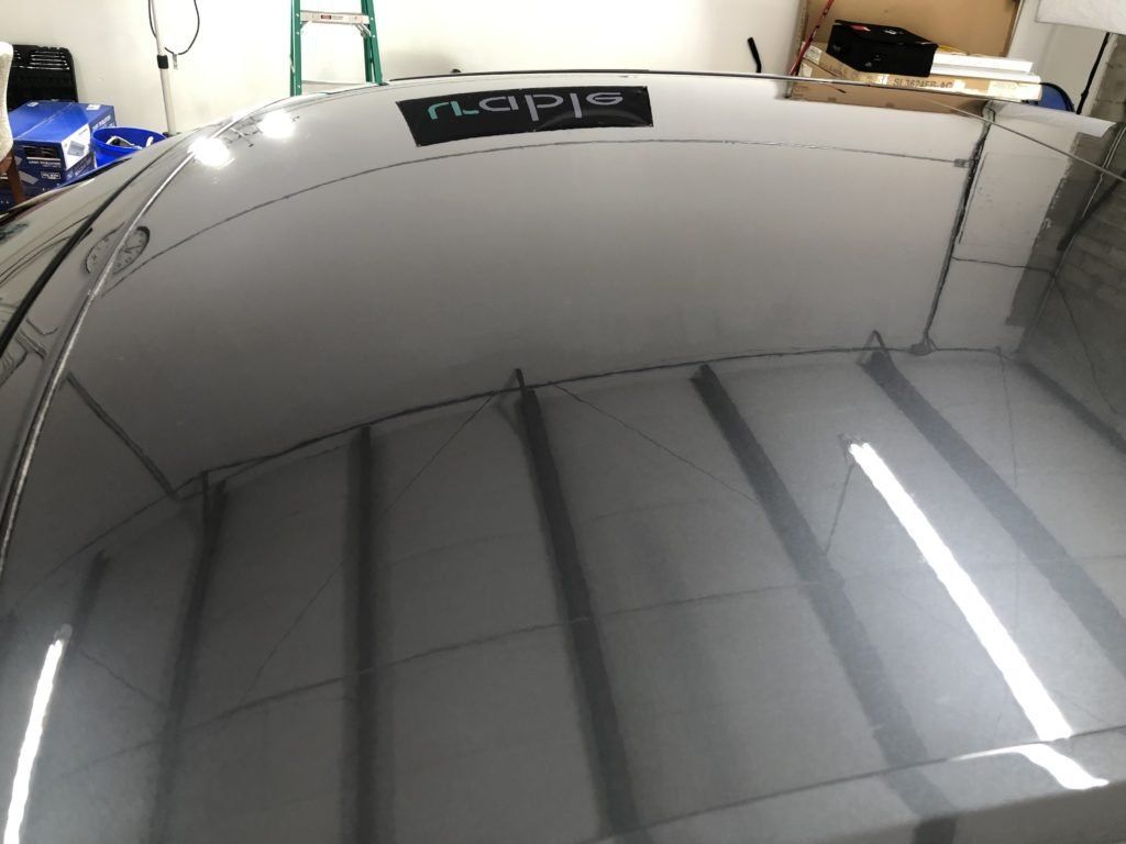 A black car 's roof is reflected in the ceiling of a garage
