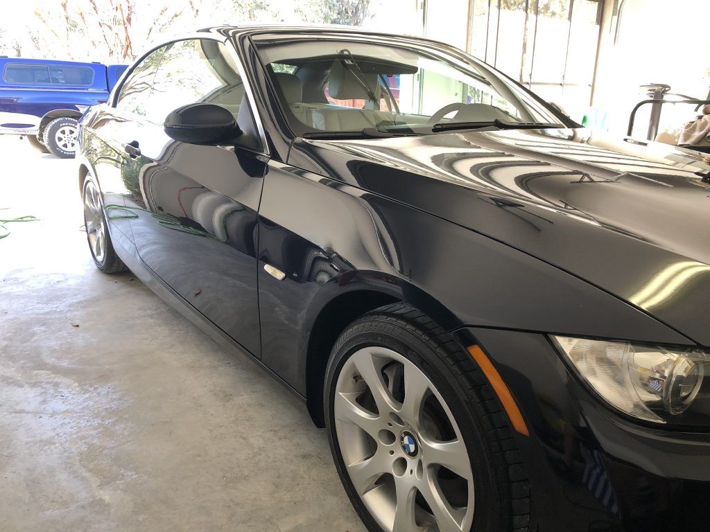 A black car is parked in a garage next to a blue truck.