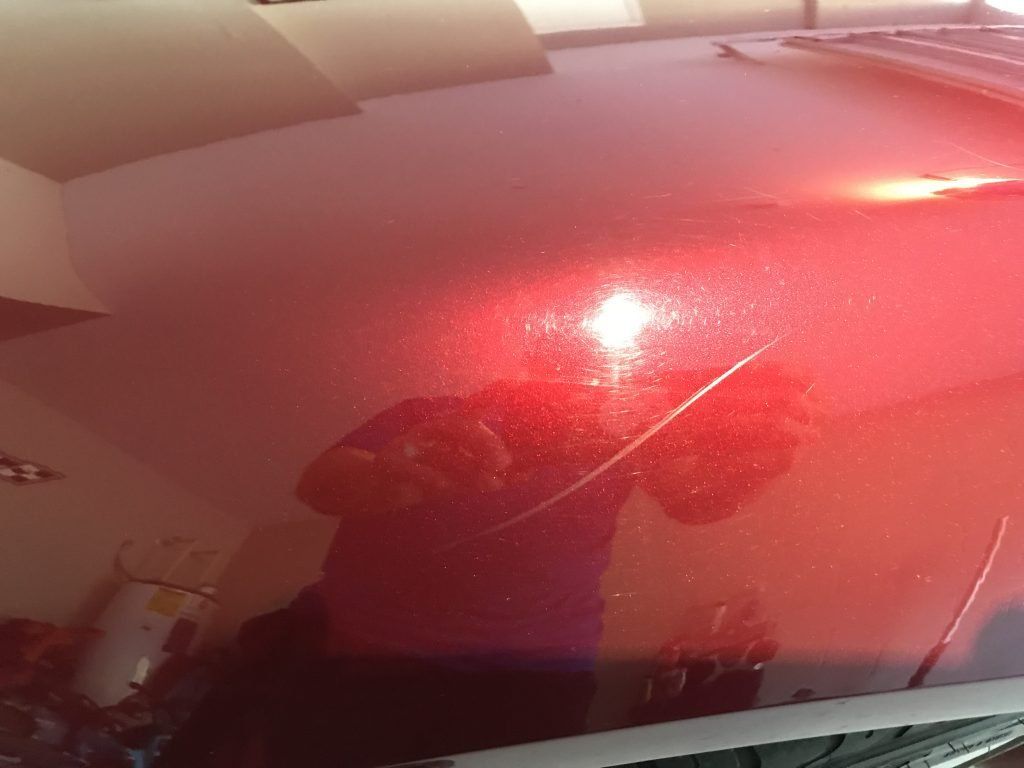 A person is taking a picture of their reflection in a red car hood.