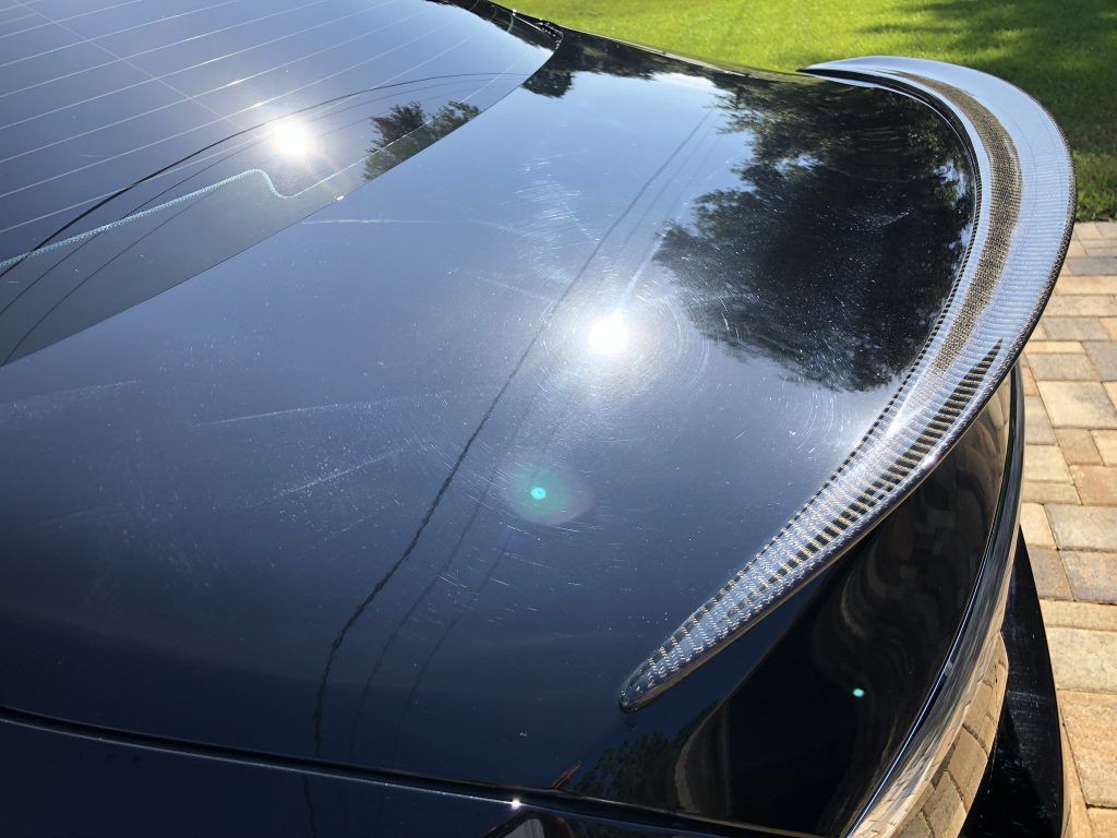A black car with a spoiler on the back is parked on a brick driveway.