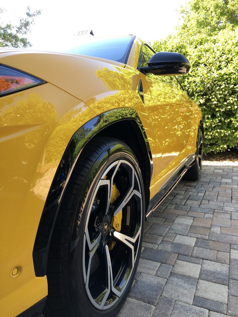 A yellow lamborghini urus is parked on a brick driveway.