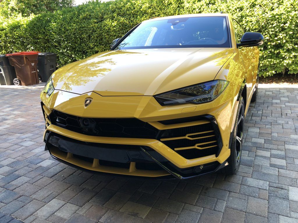 A yellow lamborghini urus is parked on a brick driveway.