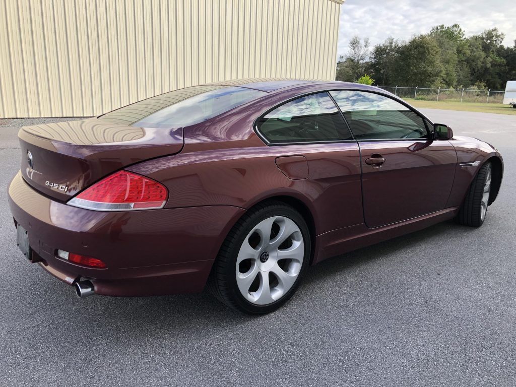 A burgundy bmw 6 series coupe is parked in front of a building.