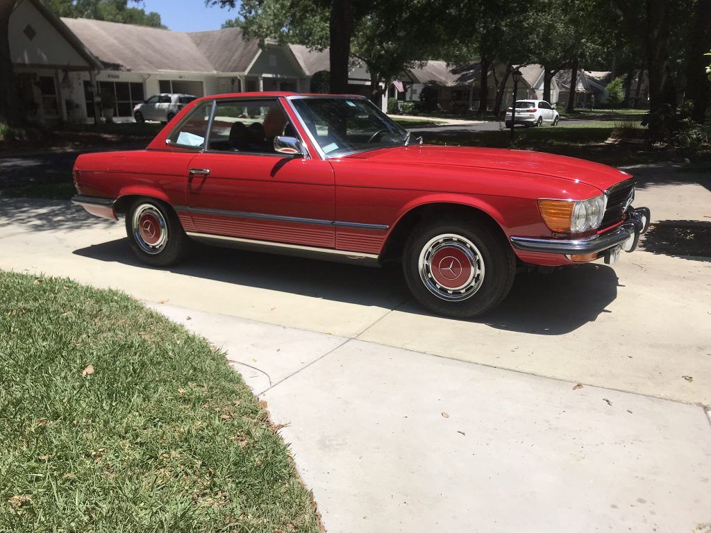 A red car is parked on the side of the road in front of a house.