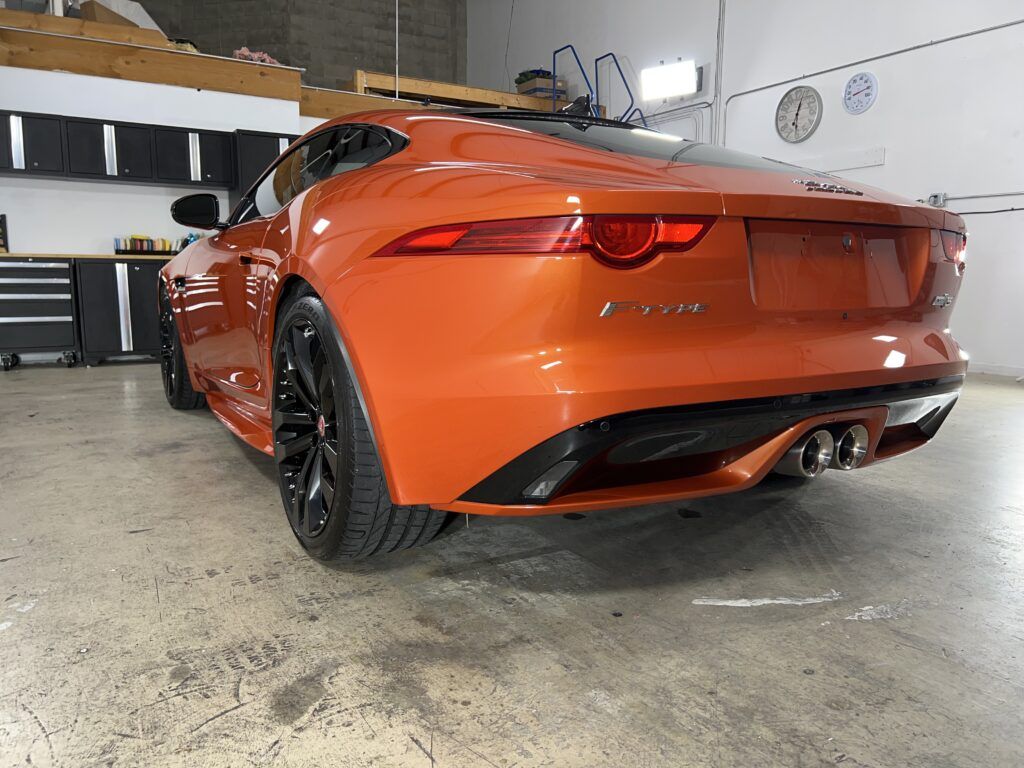 An orange jaguar f type is parked in a garage.